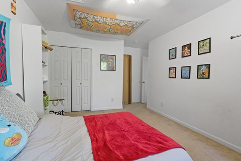 a bedroom with white walls and a red bed and a white closet